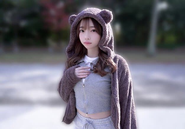 クマ耳フードの女性が屋外でグレーの服に手を添え、正面を見る