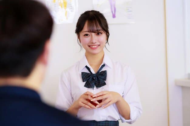 白いブラウス姿の女性がコップを両手で持ち、前を見て笑う