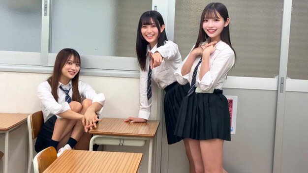 教室で制服姿の女子3人が机のそばに立ち、笑顔でこちらを見ながらゲームに誘う