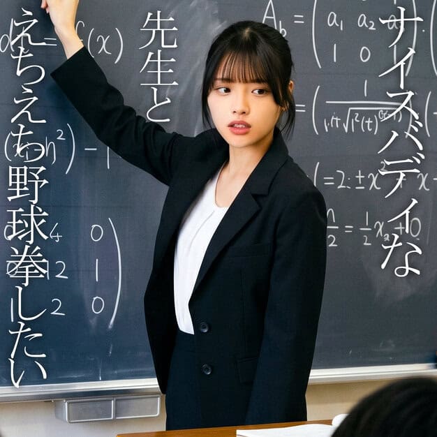 黒髪の女性が黒いスーツを着て黒板の前に立ち、右手を上げて黒板に触れている。