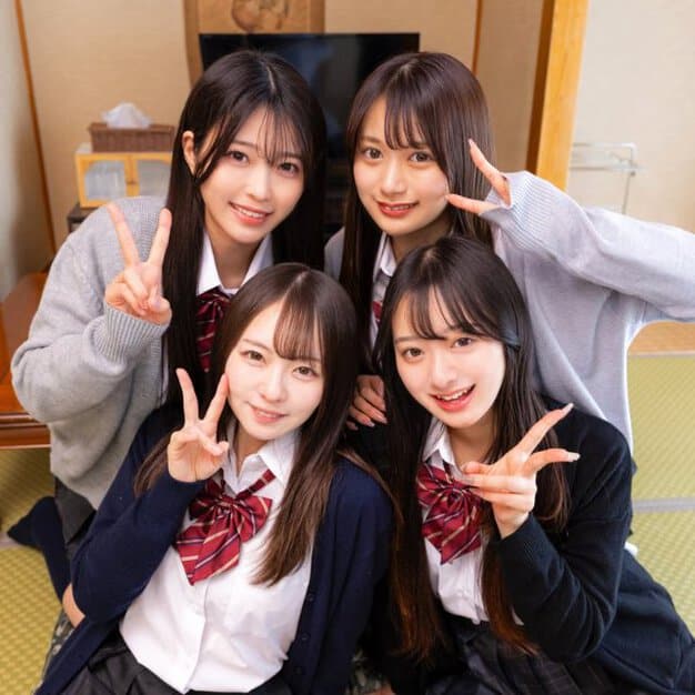 4人の女性が和室に座り、全員がピースサインをしている。後列の2人はグレーのカーディガンを着用し、前列の2人は紺色のカーディガンを着用している。背景にはテレビやタンスが見える。
