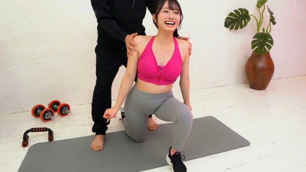 ピンクのスポーツブラ姿の黒髪女性がヨガマット上に跪き、後ろの男性に肩を掴まれている。