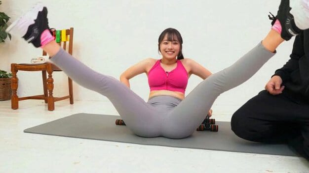 ピンクのスポーツブラ姿の黒髪女性が仰向けになり、両足を大きく開いて上げている。